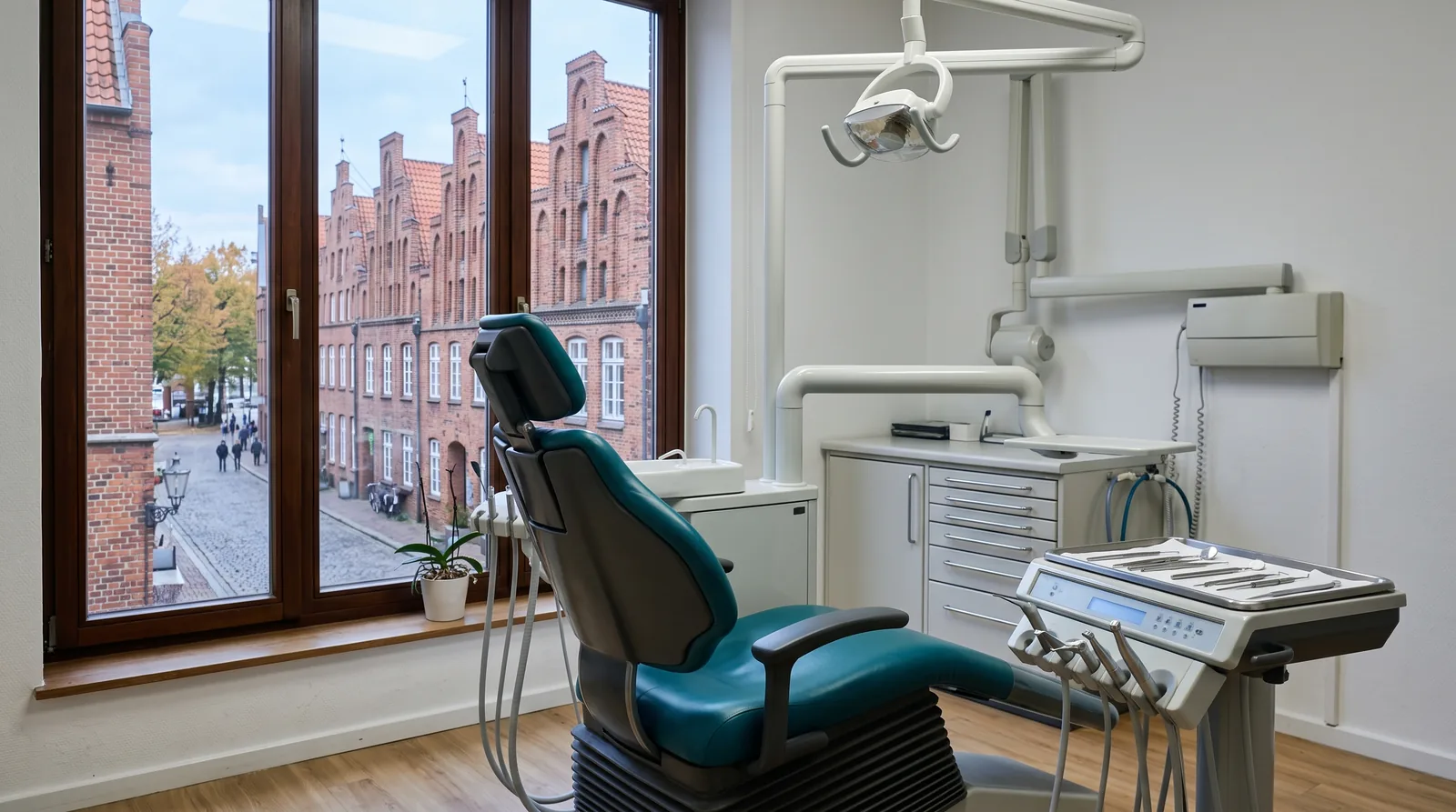Behandlungszimmer einer Zahnarztpraxis in Lübeck: Durch das Fenster sieht man rote Backsteinhäuser mit Treppengiebeln, davor ein Behandlungsstuhl und ein Instrumentenwagen.